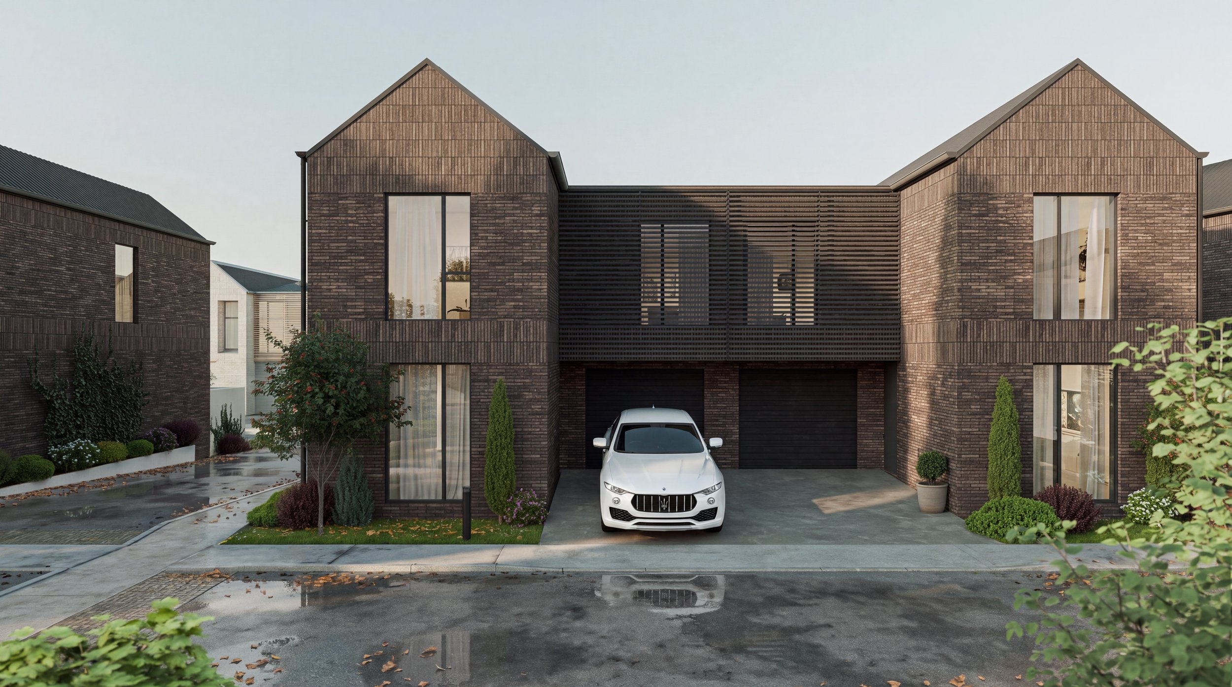 Modern two-story brick house with a white car parked in front, landscaped yard, and garage doors beneath a balcony with wooden slats, on a wet street with fallen leaves.