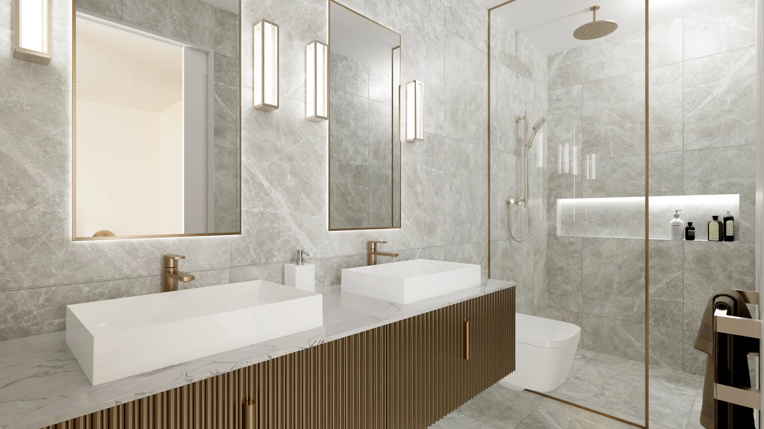 Modern bathroom with gray marble walls and gold accents. Features two rectangular vessel sinks on a marble countertop with a wood-paneled vanity. Large vertical mirrors with slim gold frames, and wall-mounted light fixtures. Walk-in shower with rain 