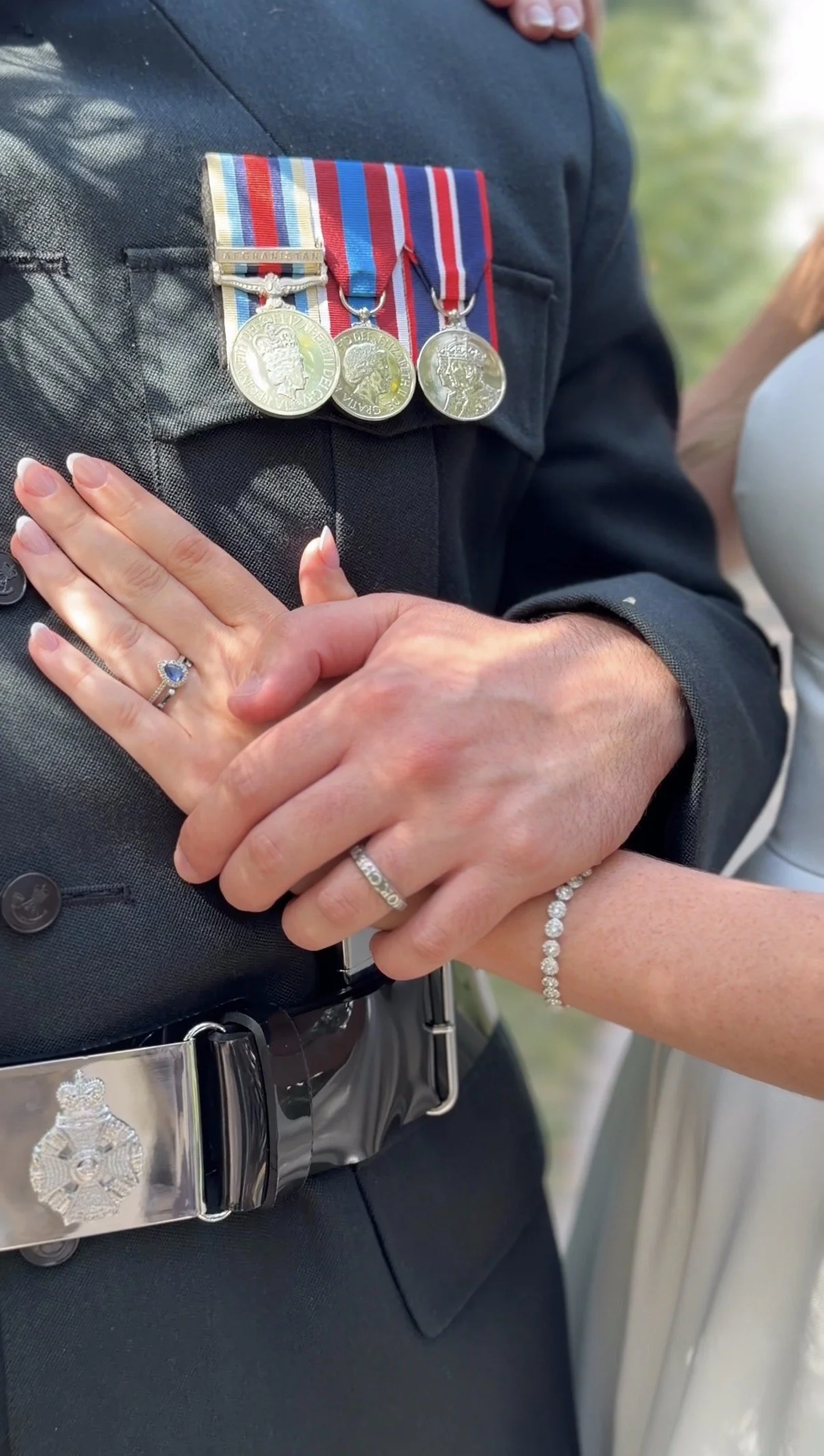 Close-up of a police officer's chest with medals and ribbons, and two hands with rings and bracelets clasped in front of the officer.