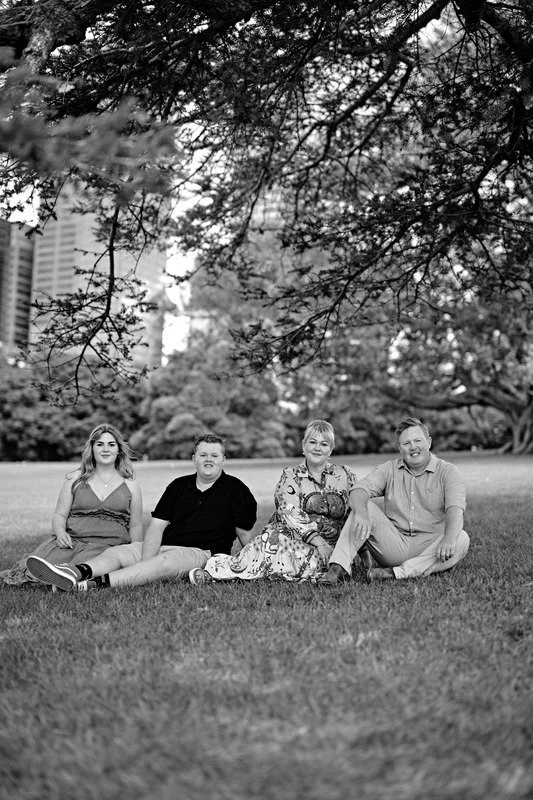 A family of four sitting on grass in a park with trees and tall buildings in the background, black and white photo.