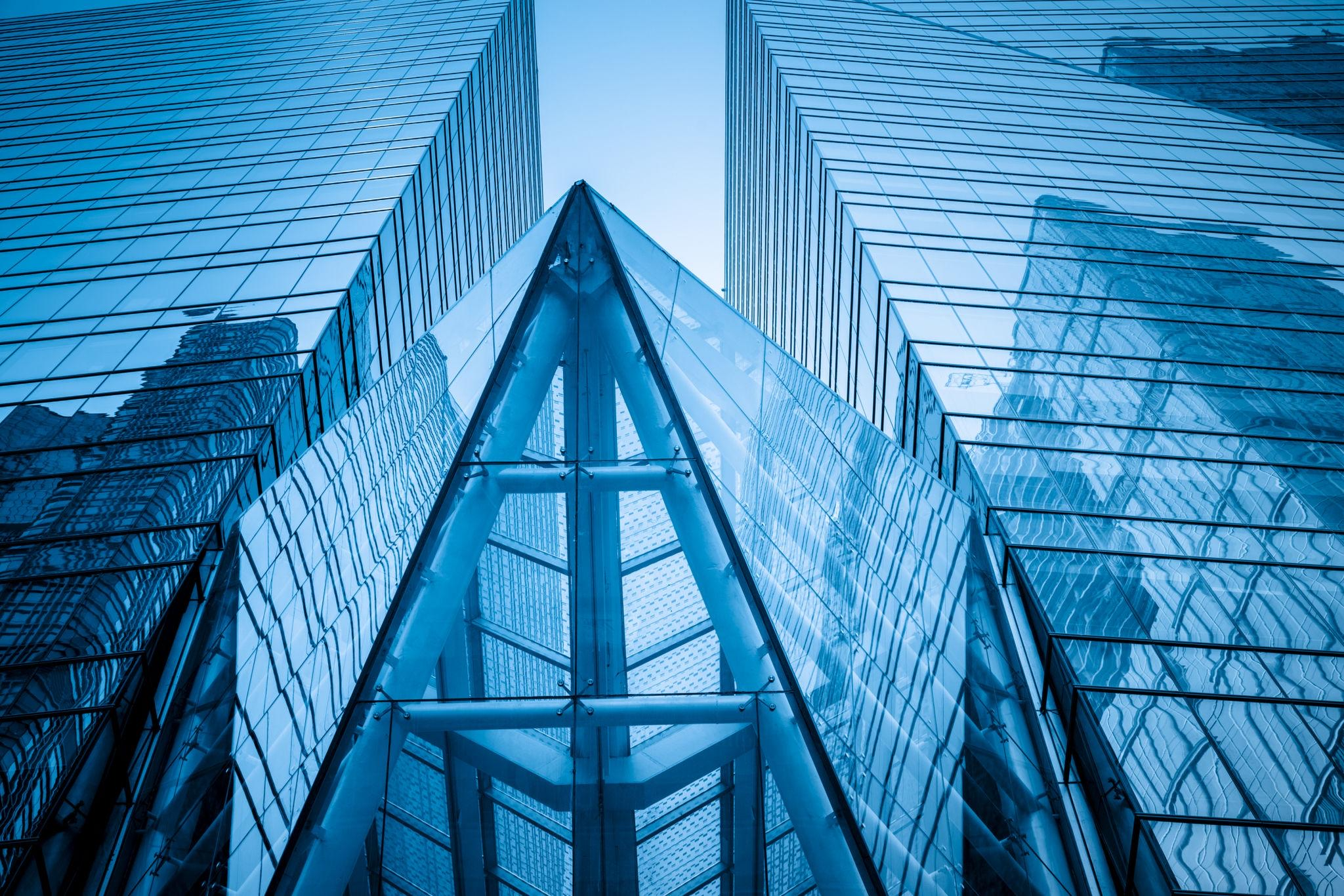 Looking up at a modern glass skyscraper with reflective windows and sharp angles.