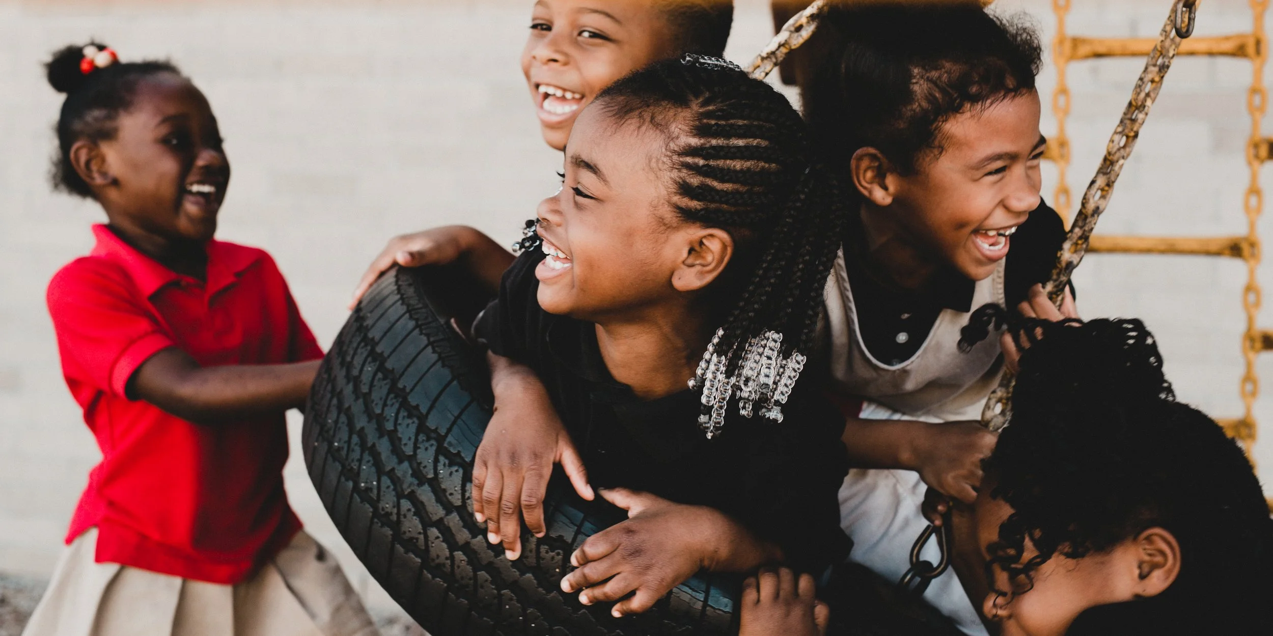 A group of children playing on a tire swing and laughing together outside.
