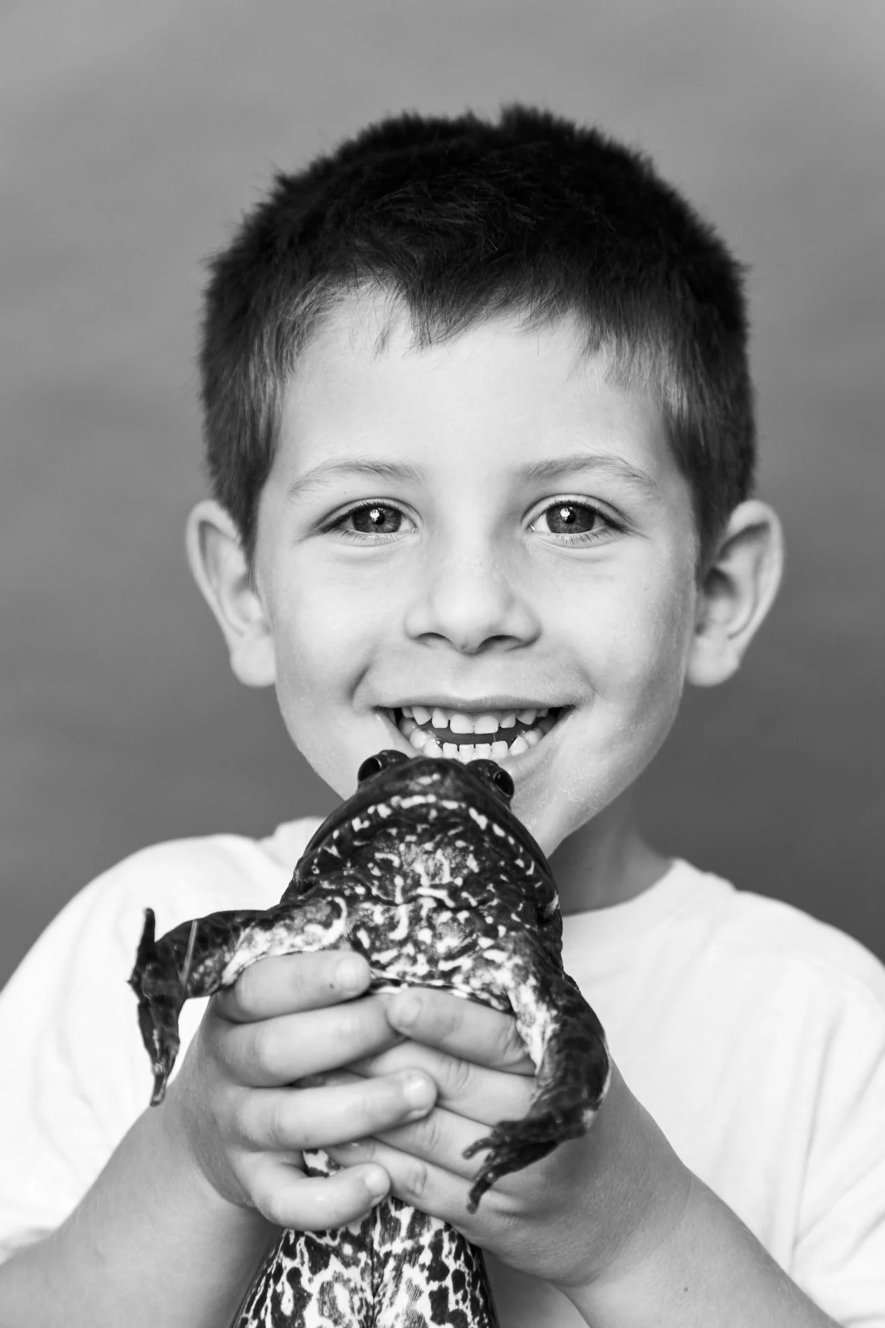 A young boy smiling and holding a large, spotted lizard
