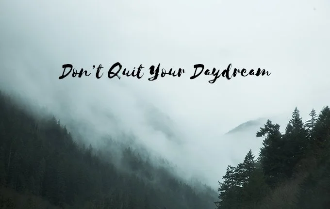 Inspirational quote 'Don't Quit Your Daydream' over a foggy mountain landscape with pine trees.