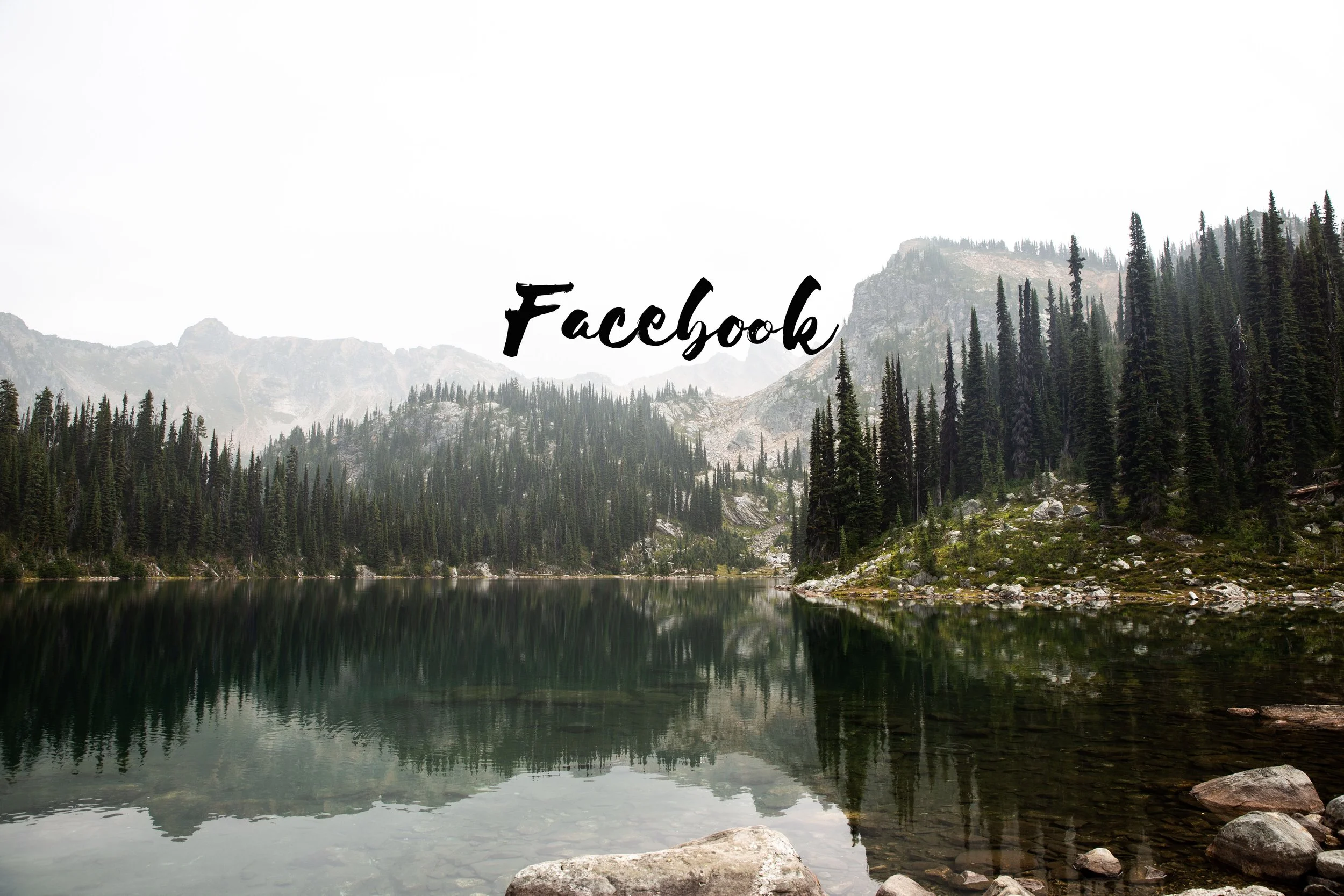 A serene mountain lake surrounded by dense evergreen forests and rugged mountain peaks in the background.