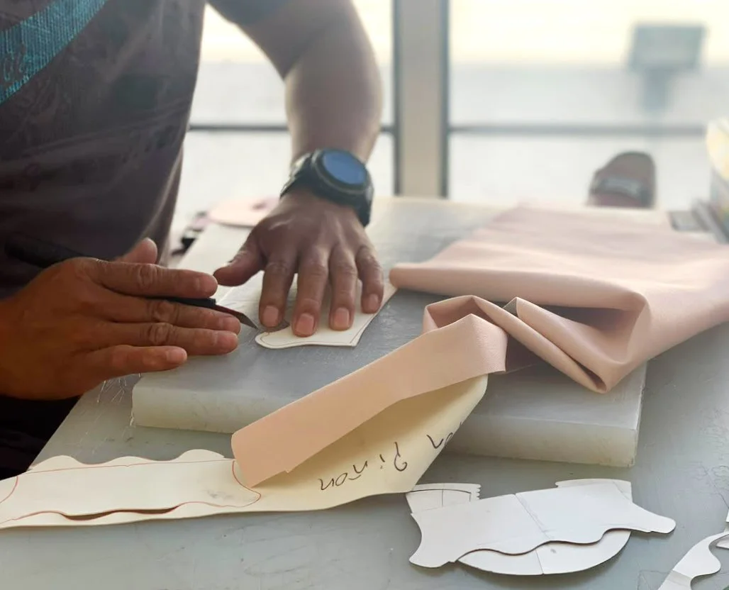 Person tracing a pattern on fabric with paper garment templates and folded pink fabric on a worktable