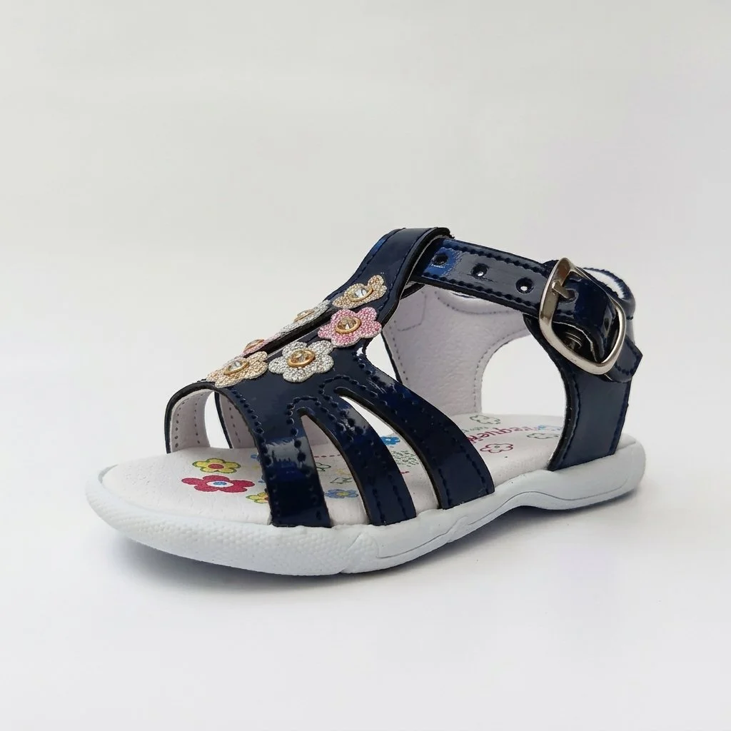 Navy blue patent girls' sandal with flower embellishments, ankle buckle strap, and white sole