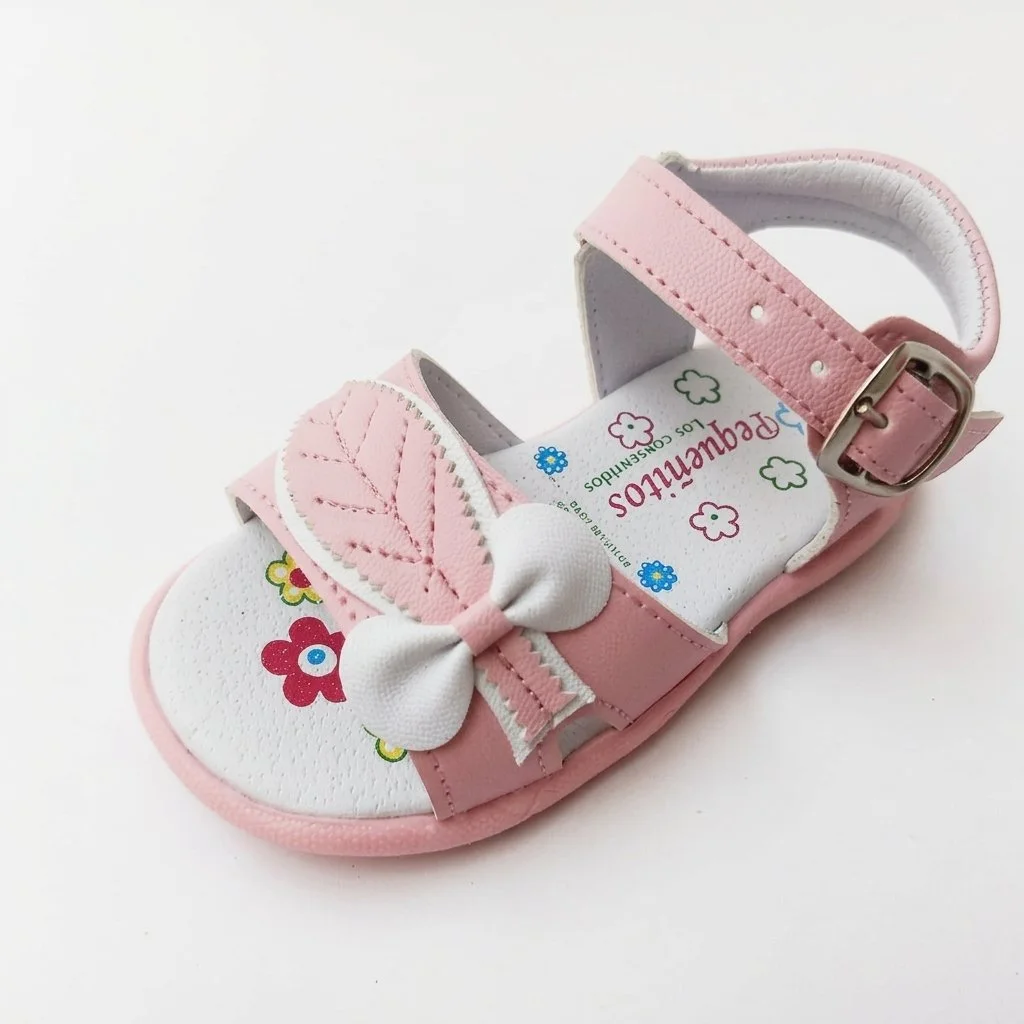 Pink children’s flower-print sandal with a bow, adjustable ankle strap, and buckle on a white background