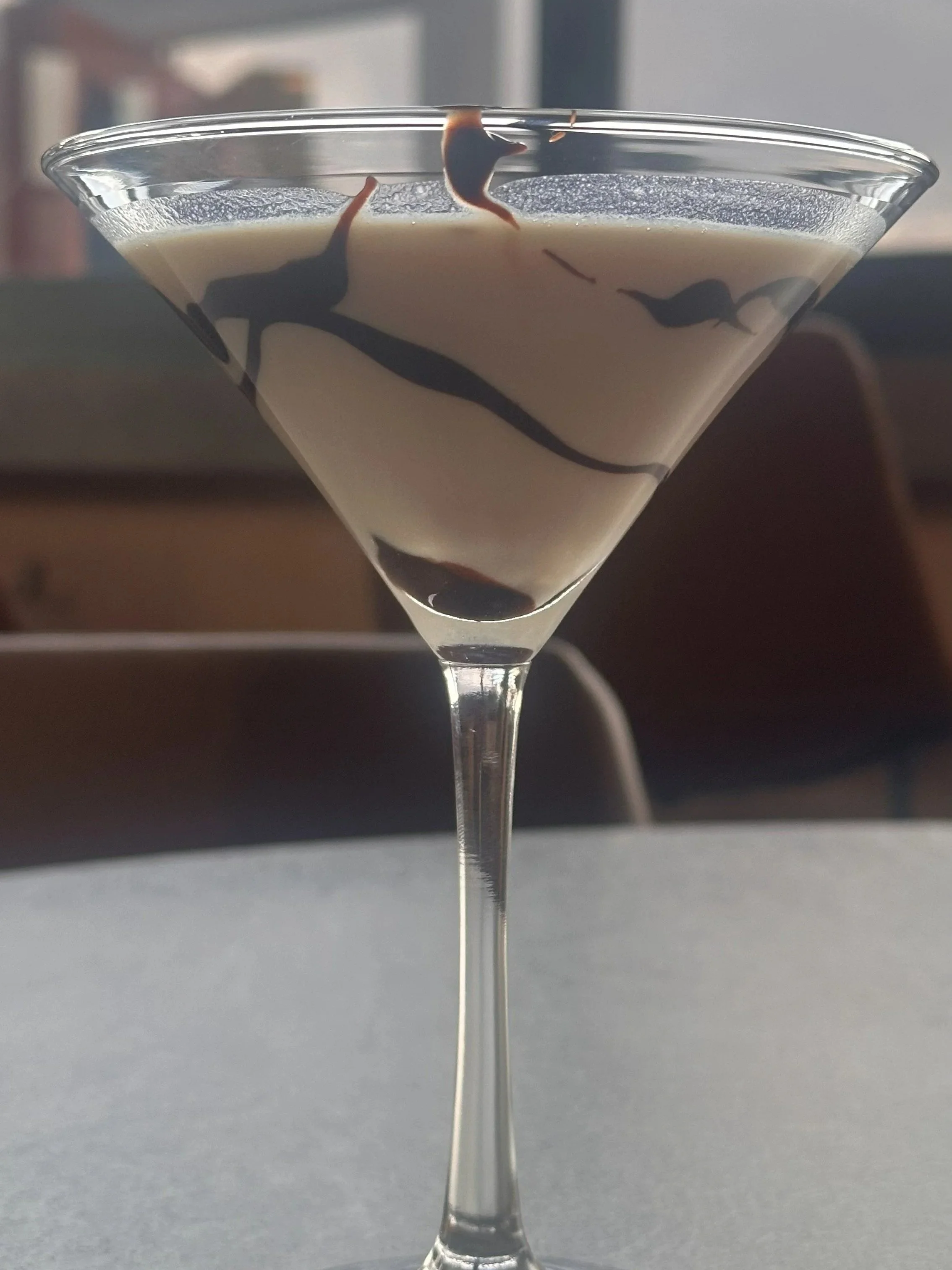 Close-up of a martini glass filled with a creamy dessert, topped with decorative chocolate or caramel drizzle.