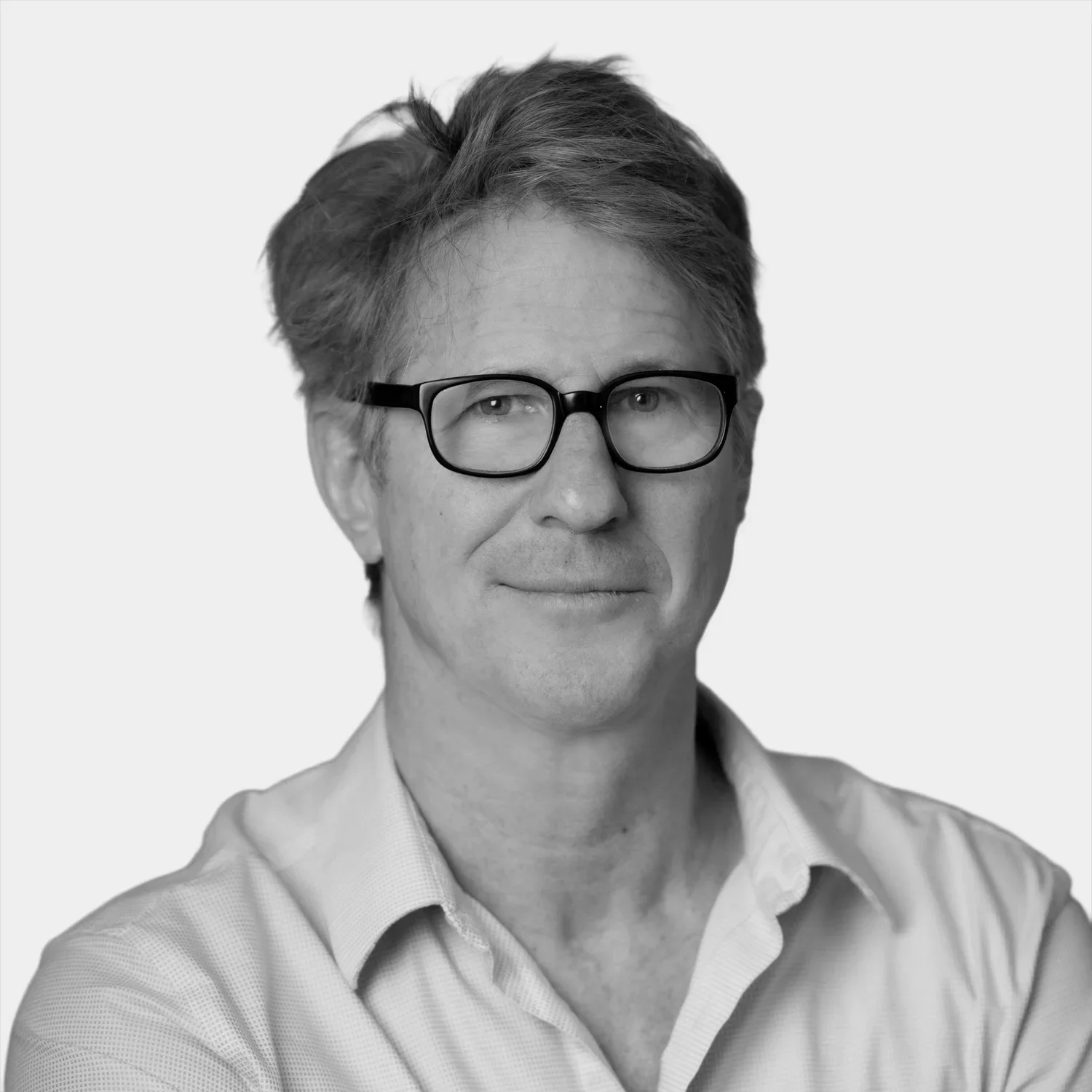 A black and white portrait of a middle-aged man with glasses, short tousled hair, wearing a collared shirt.
