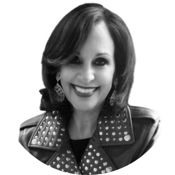 A woman with shoulder-length hair smiling, wearing earrings and a studded leather jacket.