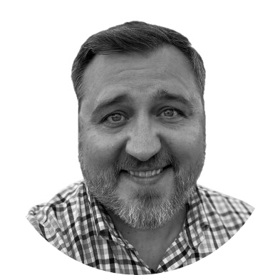 Black and white portrait of a smiling man with a beard, wearing a checkered shirt.