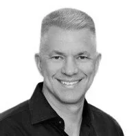 Black and white headshot of a smiling man with short gray hair, wearing a dark shirt.