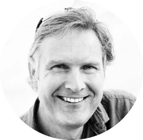 Black and white portrait of a smiling man with short, wavy hair, wearing a casual shirt.