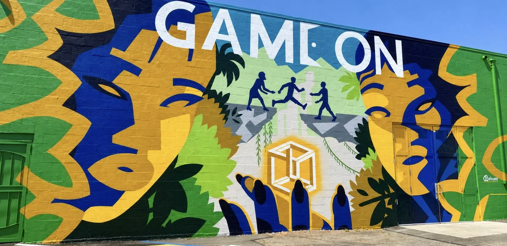 Colorful outdoor mural with the word 'GAMON' at the top, featuring silhouettes of people dancing or playing, surrounded by abstract greenery, leaves, and shapes in yellow, green, blue, black, and white.