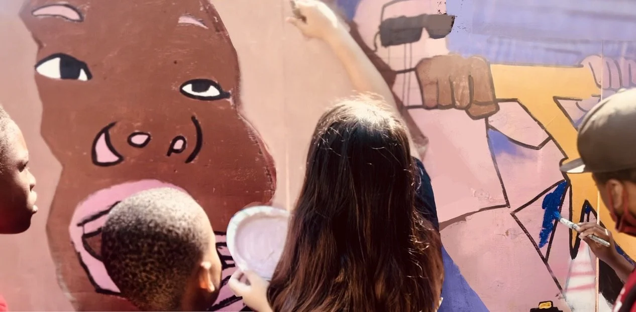Group of children are painting a colorful mural on a wall, featuring a cartoon-style pig face and abstract shapes.
