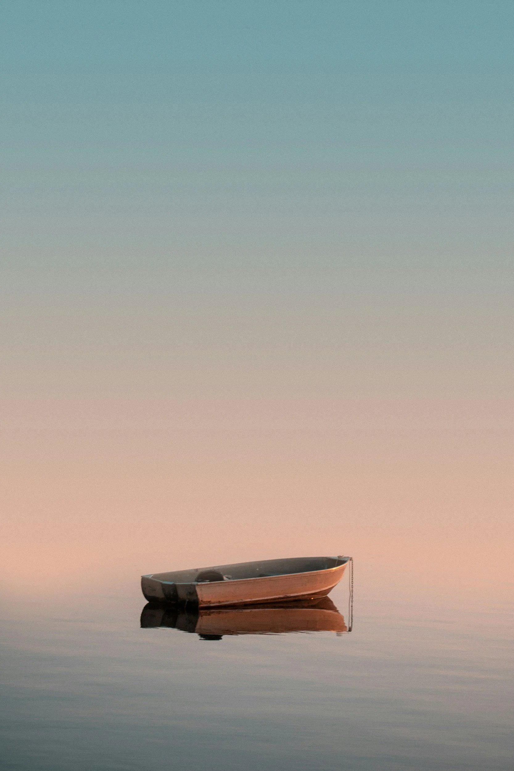 A small boat floating on calm water at sunset with a pastel sky.