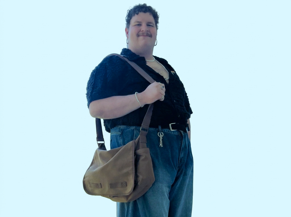 Person with curly hair and earrings carrying a brown shoulder bag, wearing a black top and blue jeans, against a plain light background.