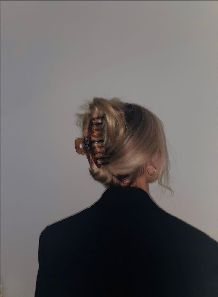 A person with blonde hair in curlers, wearing a dark jacket, facing away from the camera against a plain background.