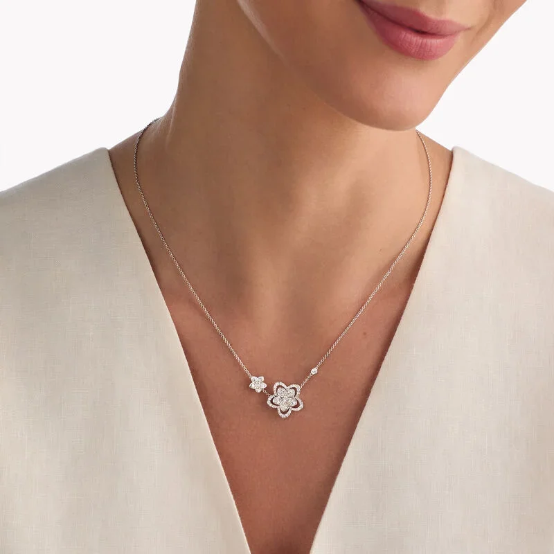 Close-up of a woman's neck wearing a silver floral necklace with small diamonds, against a white V-neck blouse.