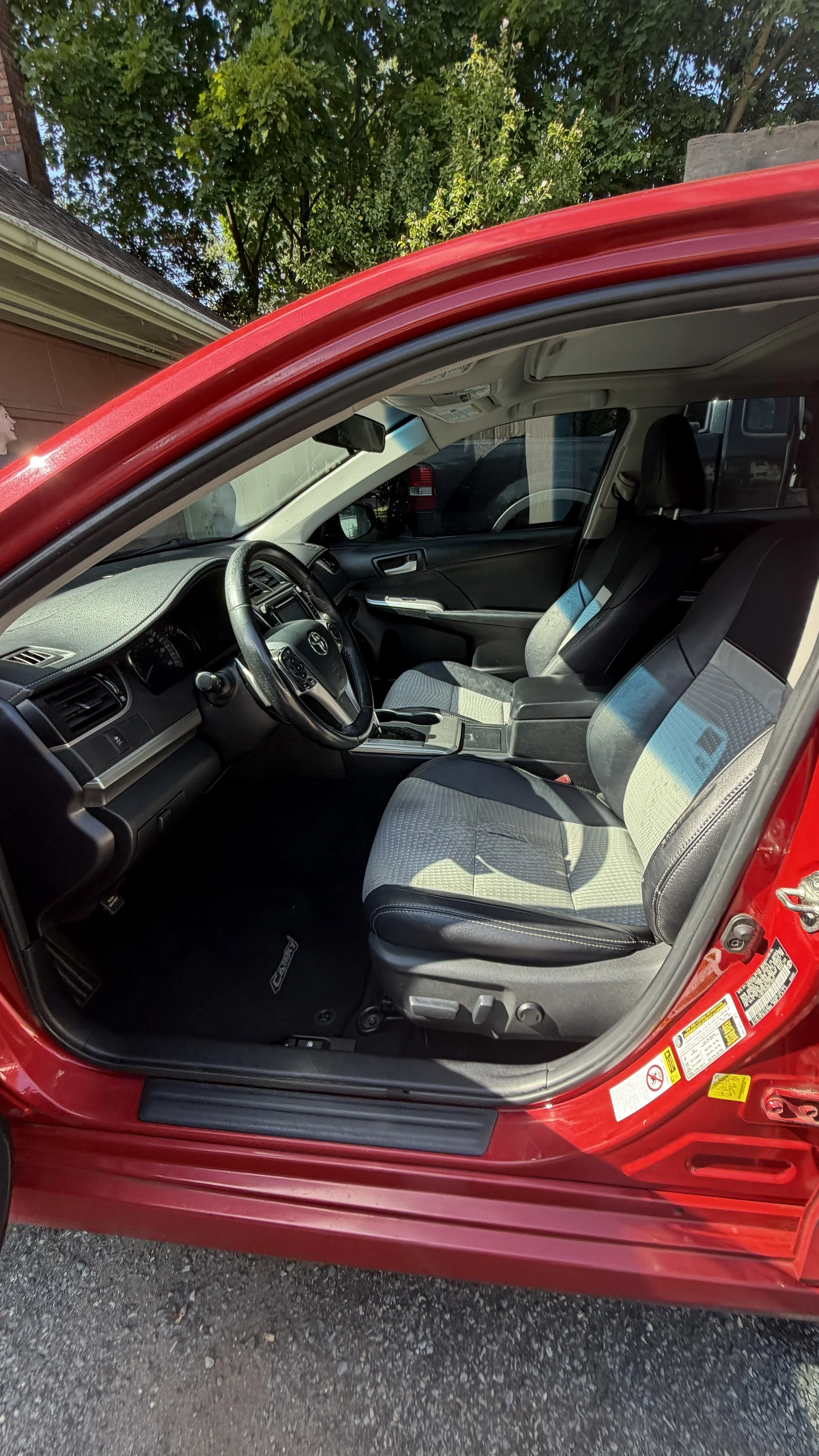 Interior of a red car showing the driver's seat, passenger seat, and dashboard with a view through the open door.