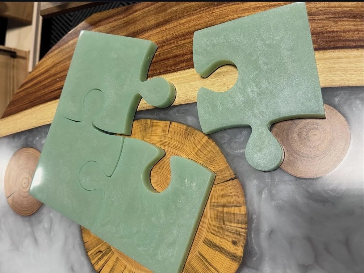 Three green jigsaw puzzle pieces on a wooden surface with circular wood accents and a woven wood piece.