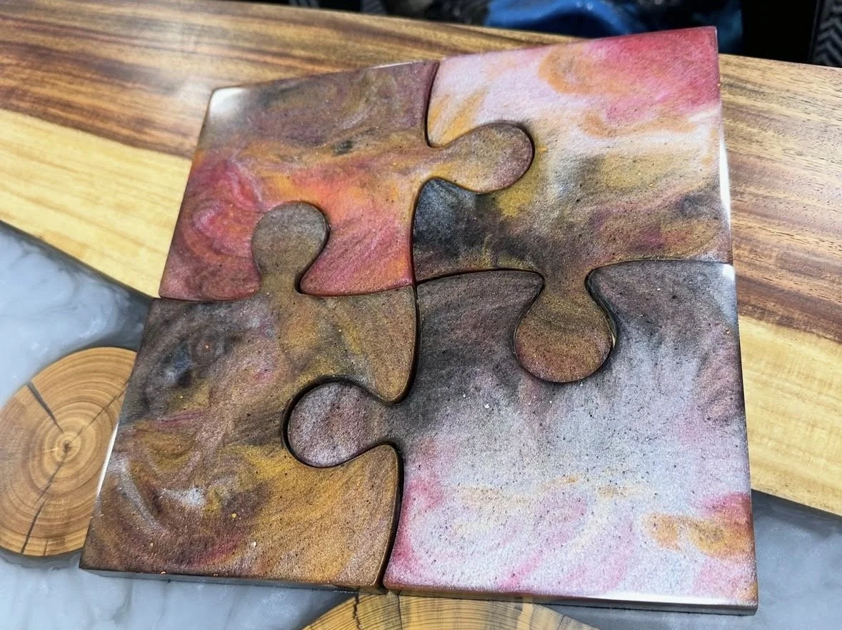 Four interconnected puzzle pieces with a marbled, colorful pattern in shades of pink, yellow, brown, and black.
