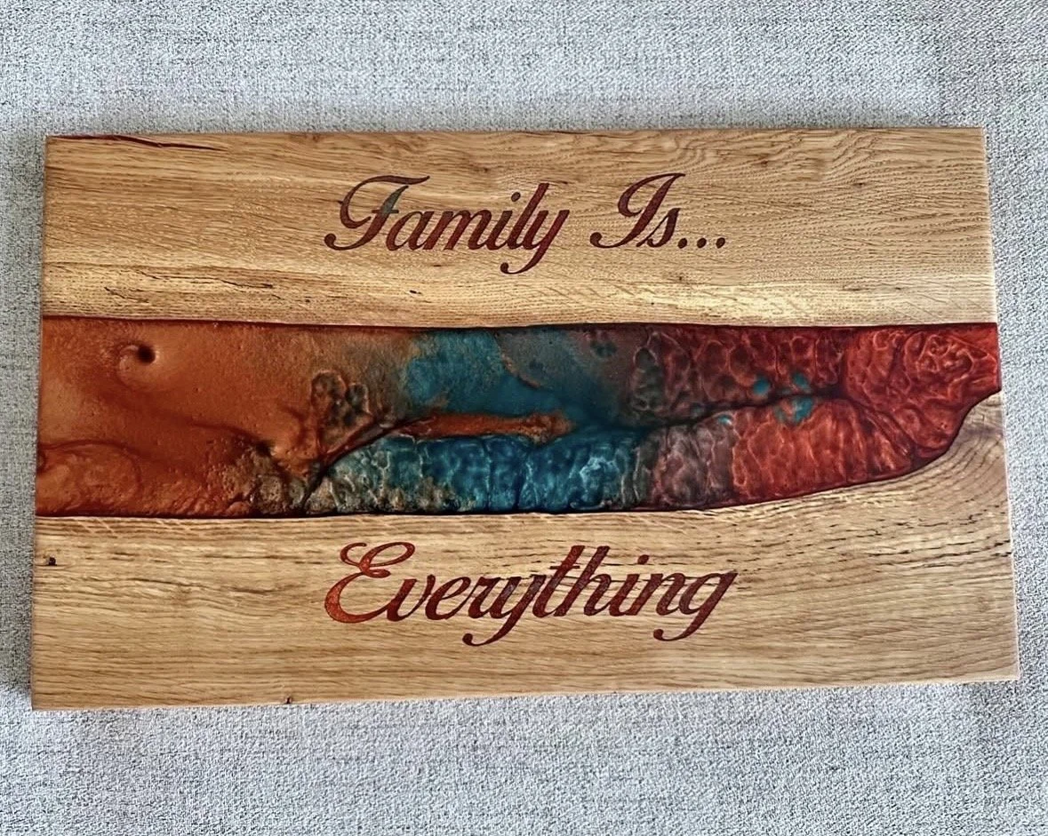 A wooden board with the engraving 'Family Is... Everything' and a colored epoxy resin river running through the center.