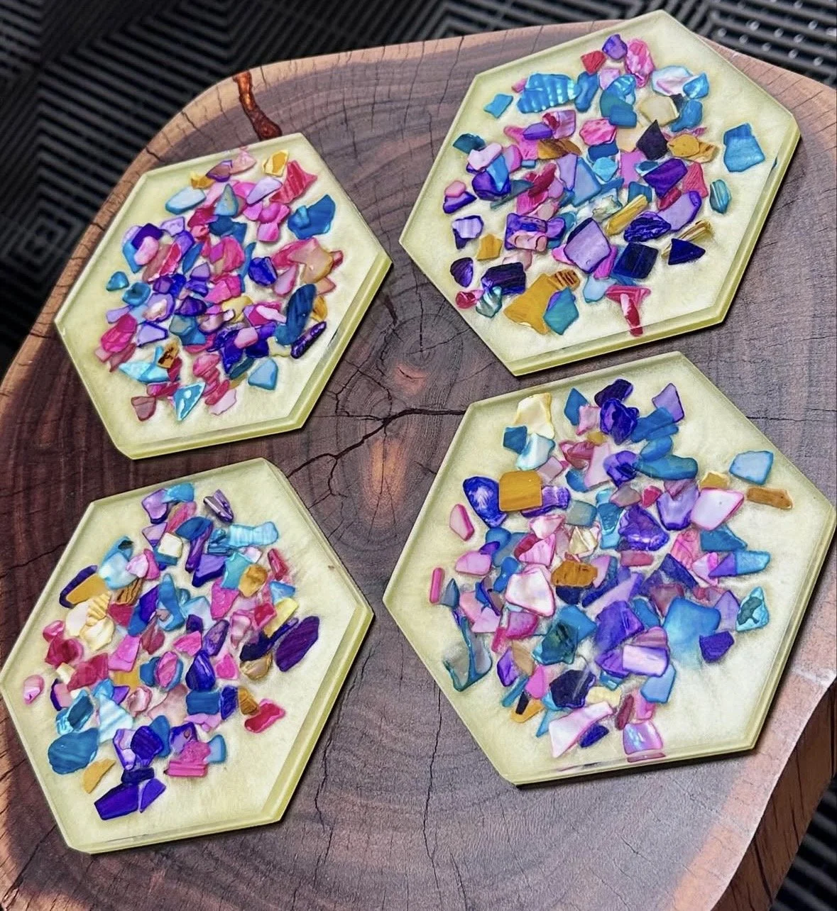 Four yellow hexagonal dishes filled with colorful broken glass pieces on a wooden surface.
