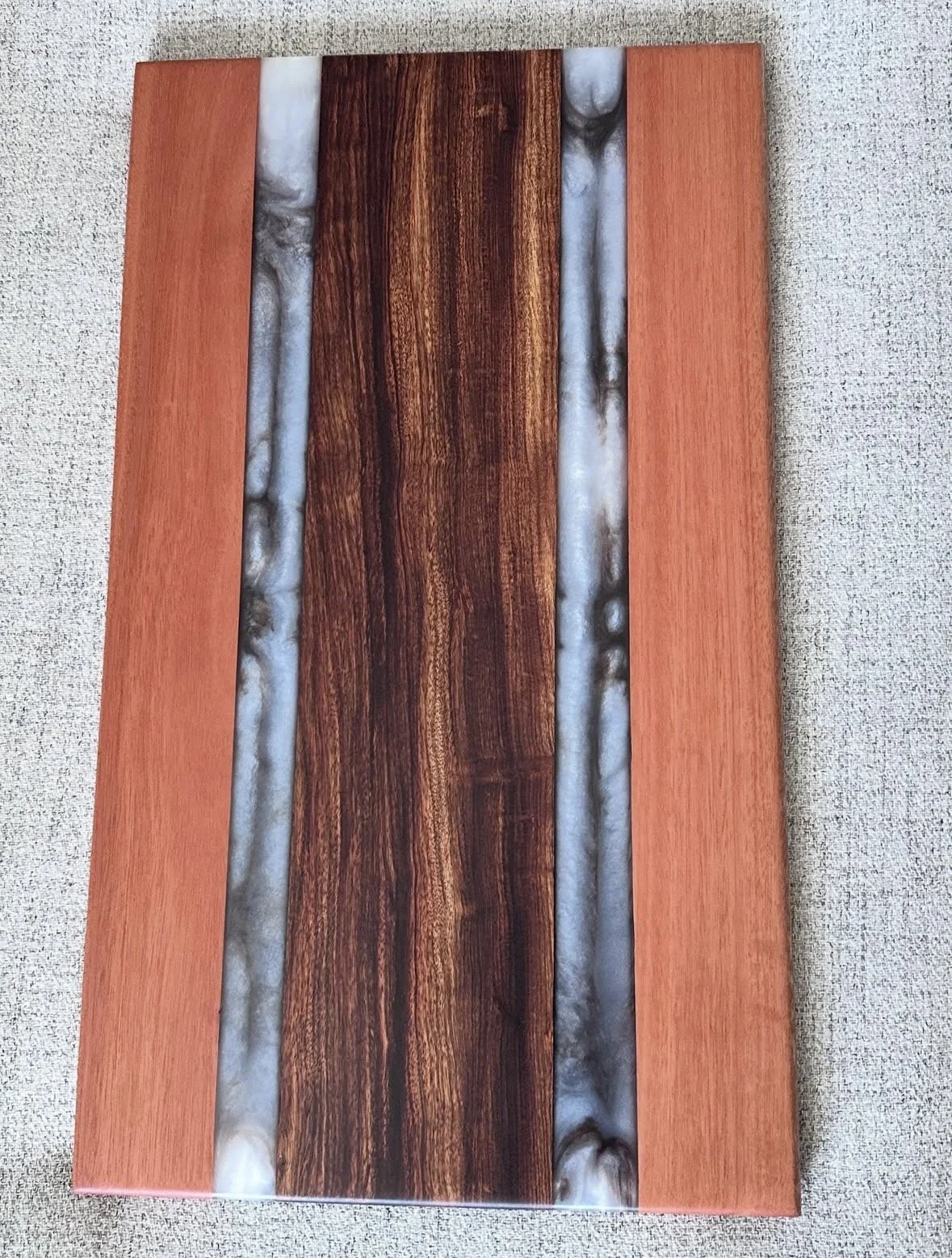 Close-up of a wooden table with a central dark wood panel surrounded by lighter wood and resin inlays.