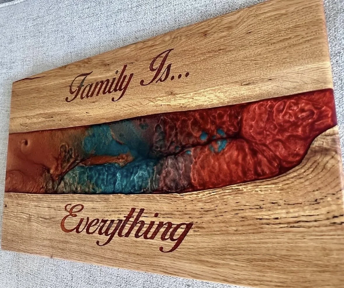A wooden plaque with the words 'Family Is... Everything' engraved and painted in cursive, featuring a colorful, textured river-like design in the middle.