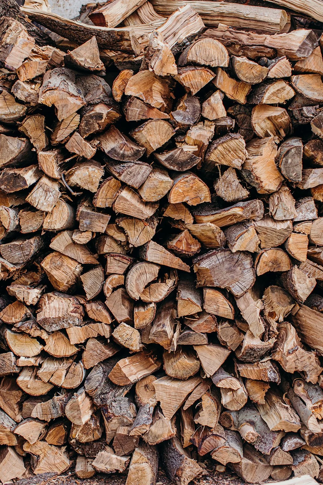 Stacked firewood logs with split and charred surfaces in varied shapes and sizes.