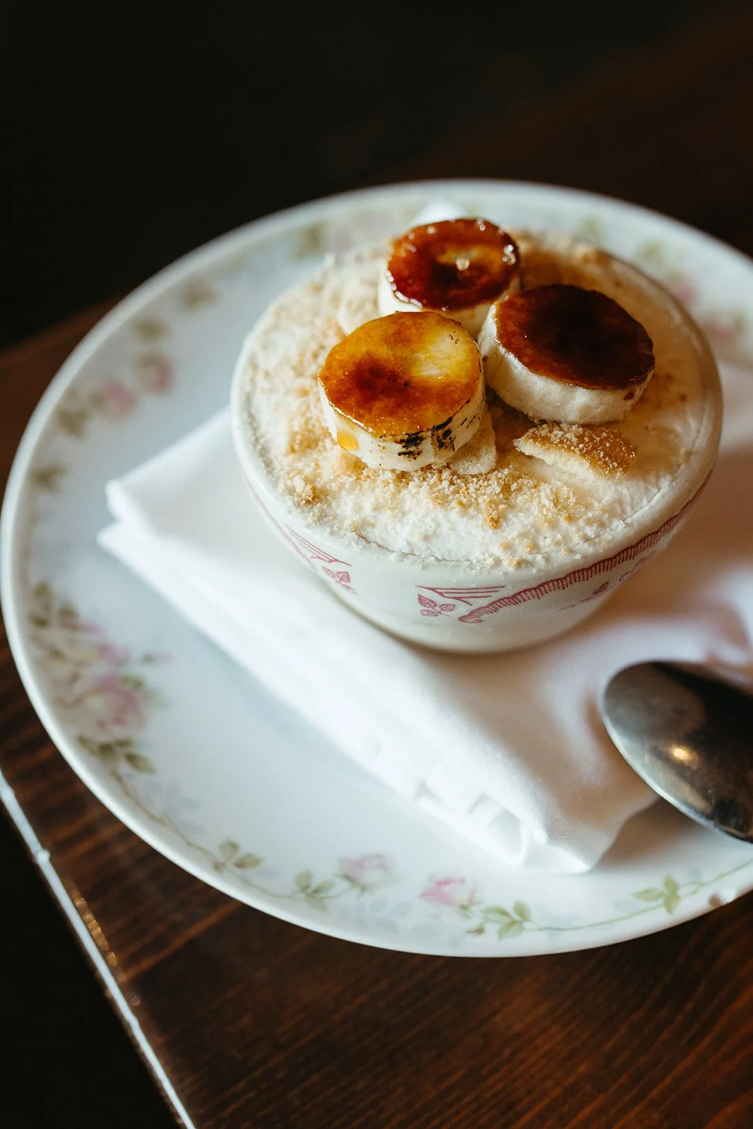 Banana pudding, served on a floral plate with a napkin and spoon.
