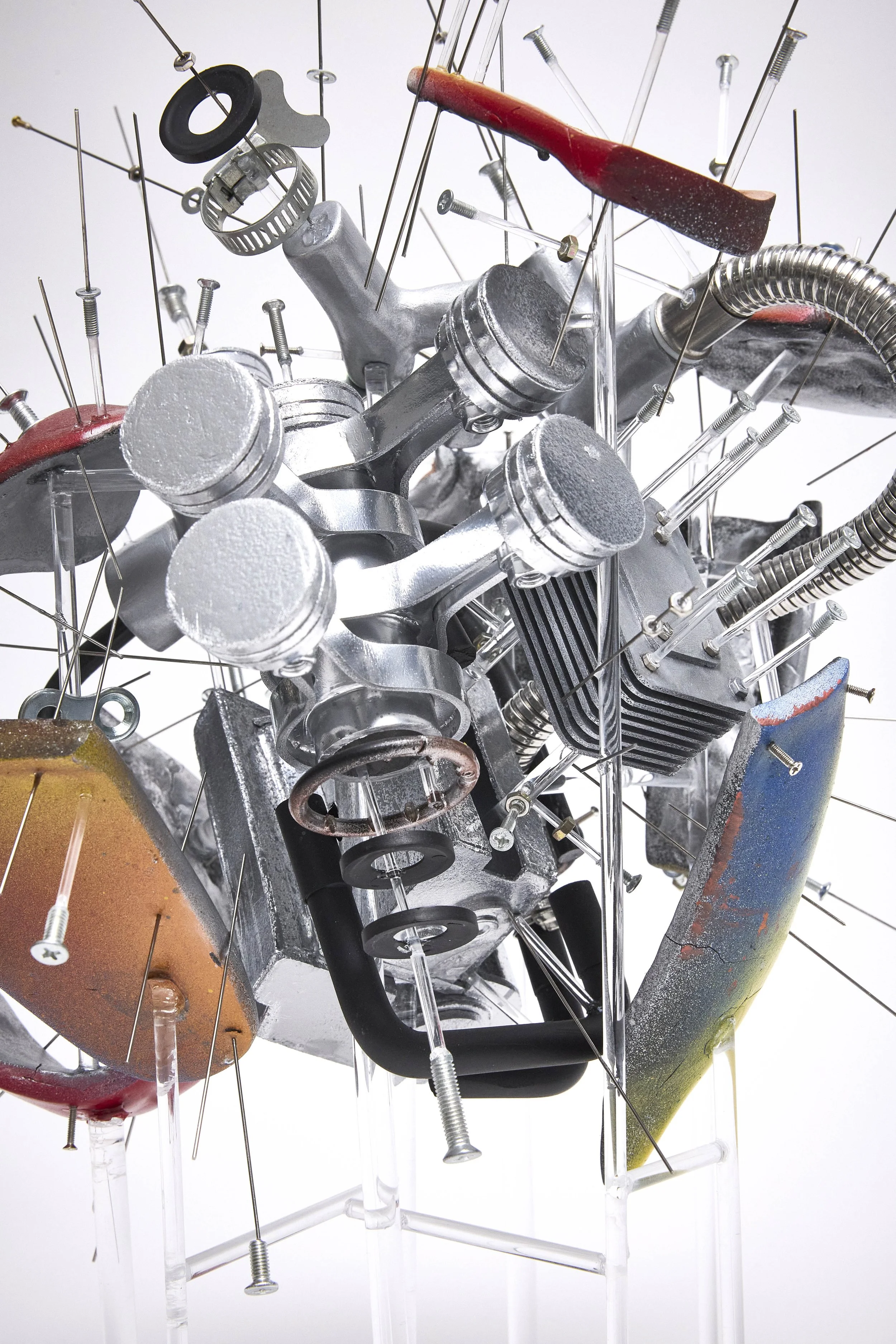 Contemporary sculpture made of metal and glass with various mechanical and industrial components like pistons, screws, pipes, and wires arranged in a complex, abstract structure.