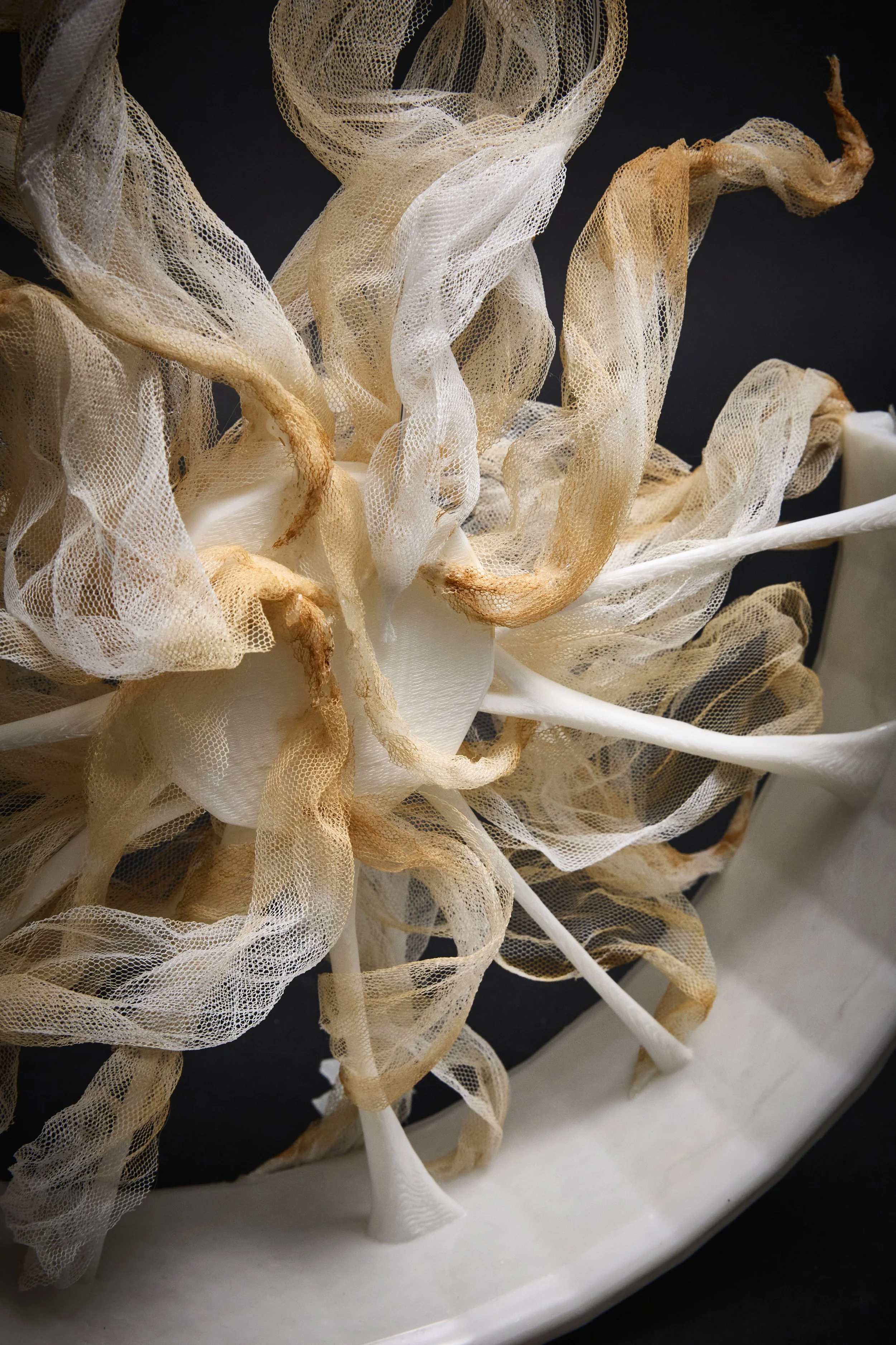 Close-up of intricately woven beige and white mesh fabric with ruffled textures on a dark background.