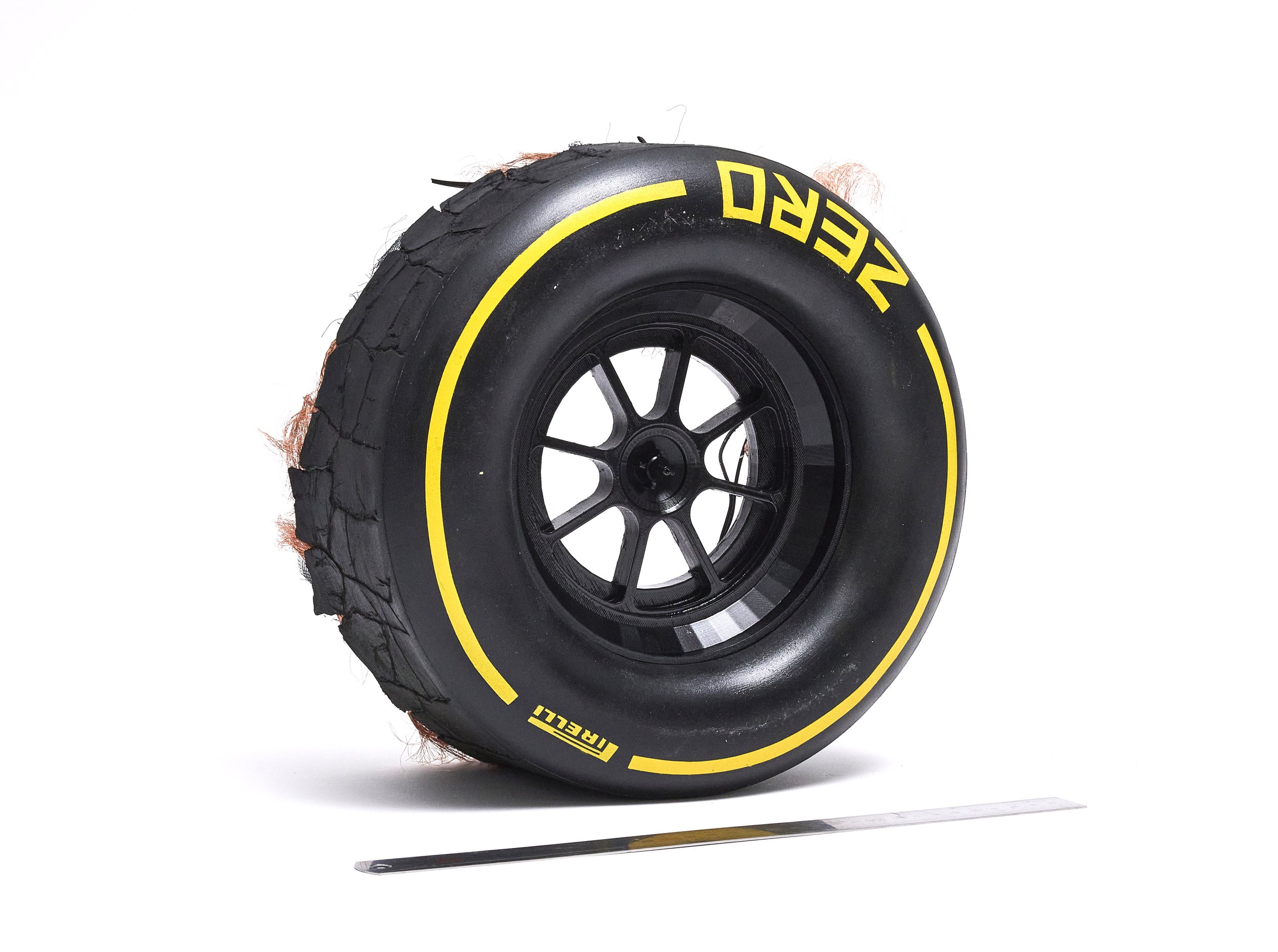 A racing tire with a black wheel, yellow markings, and a cracked outer rubber, mounted on a white background.