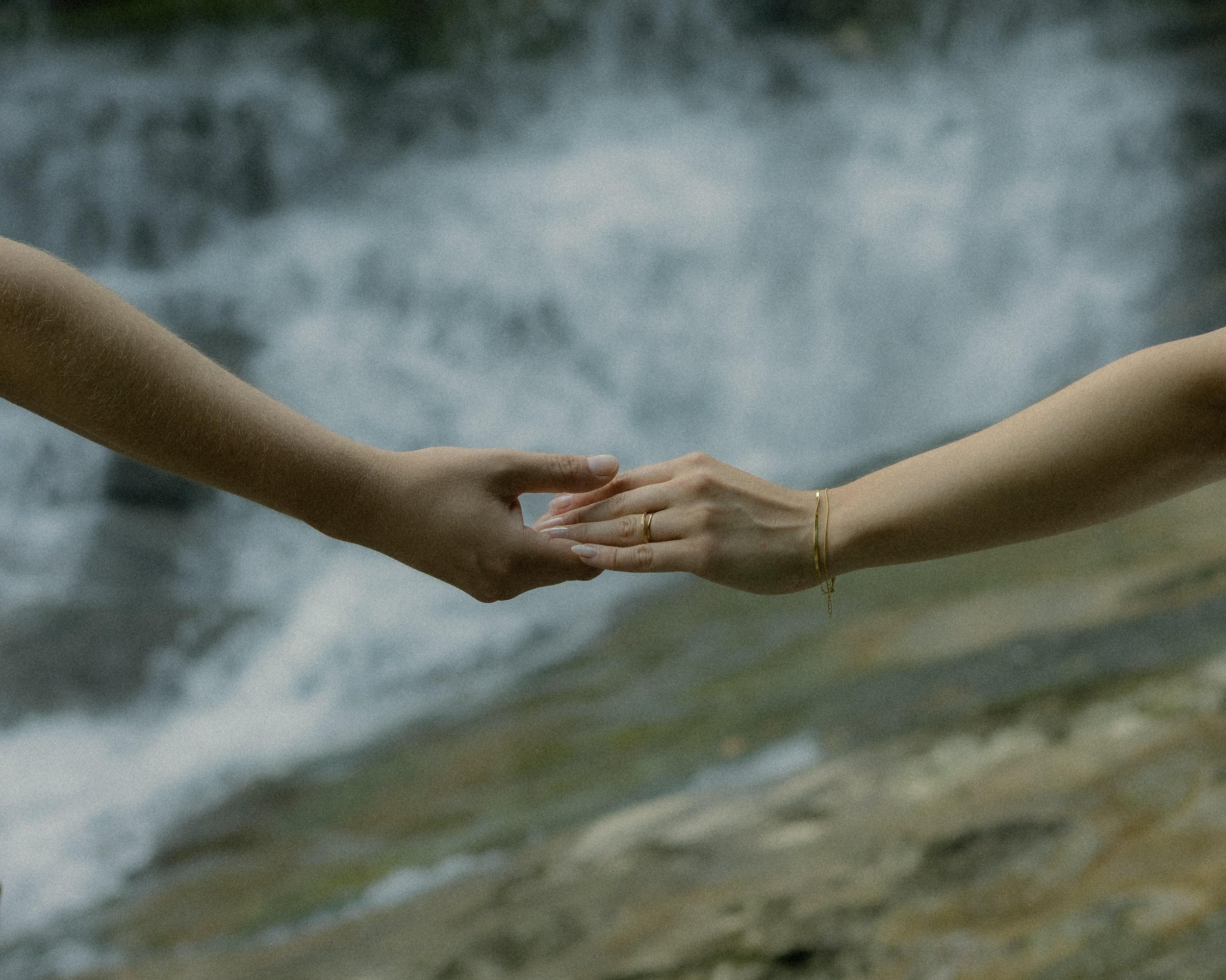 Nahaufnahme einer Hand, die eine andere hält, vor dunklen, wolkigen Himmel.