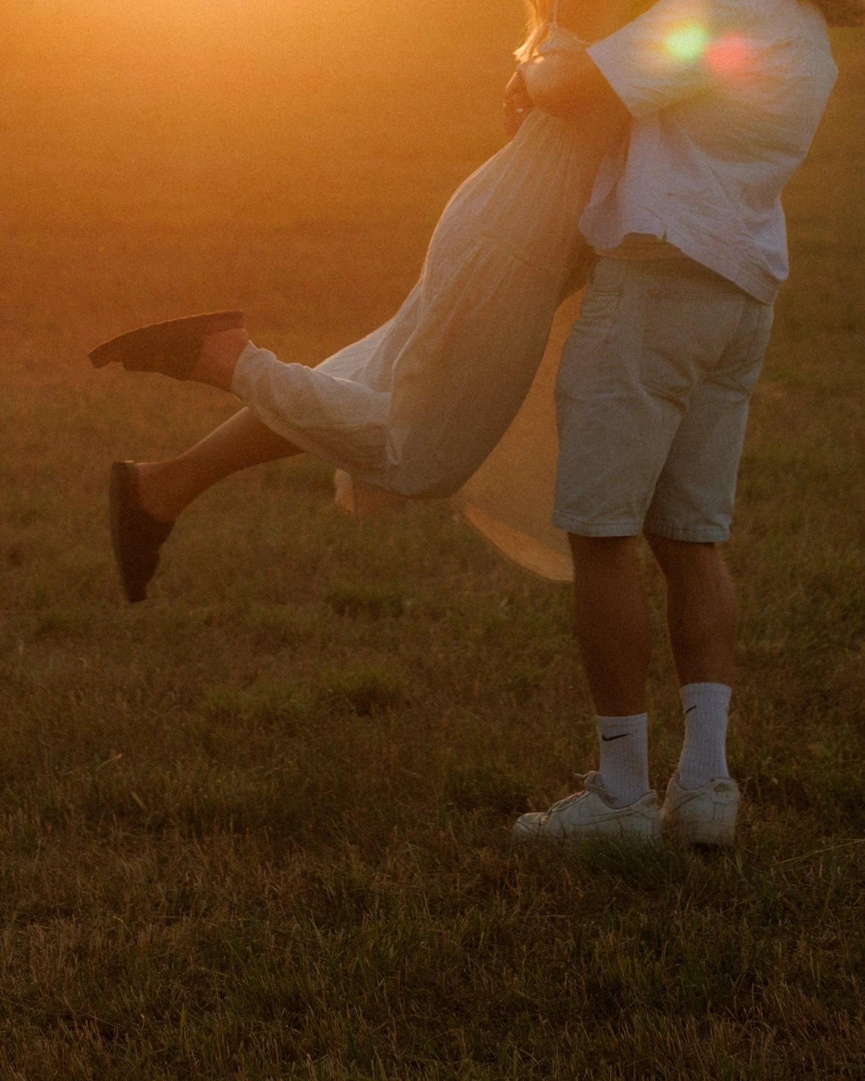 Ein Paar tanzt im Sonnenuntergang auf einem Feld, beide tragen weiße Kleidung.