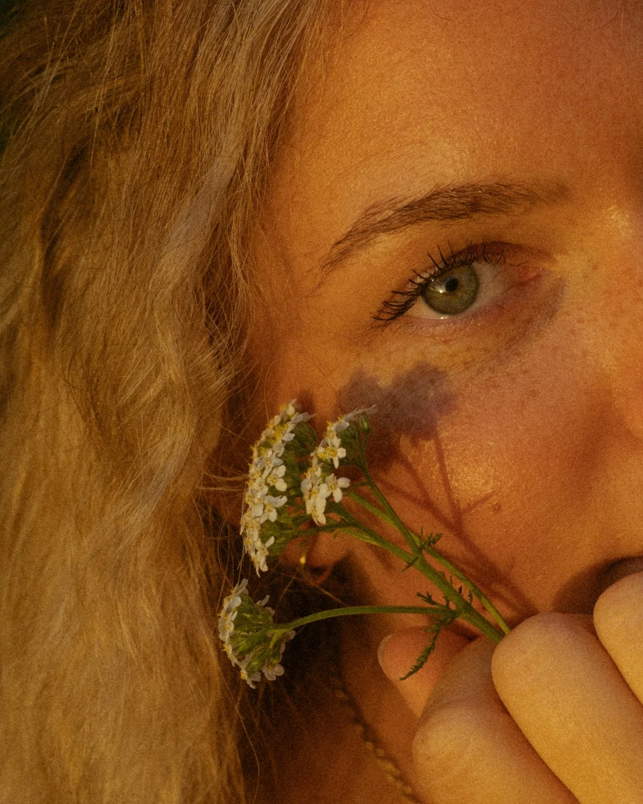 Nahaufnahme eines Mädchengesichts mit blauer Auge, das ein kleines Blumenbouquet hält.