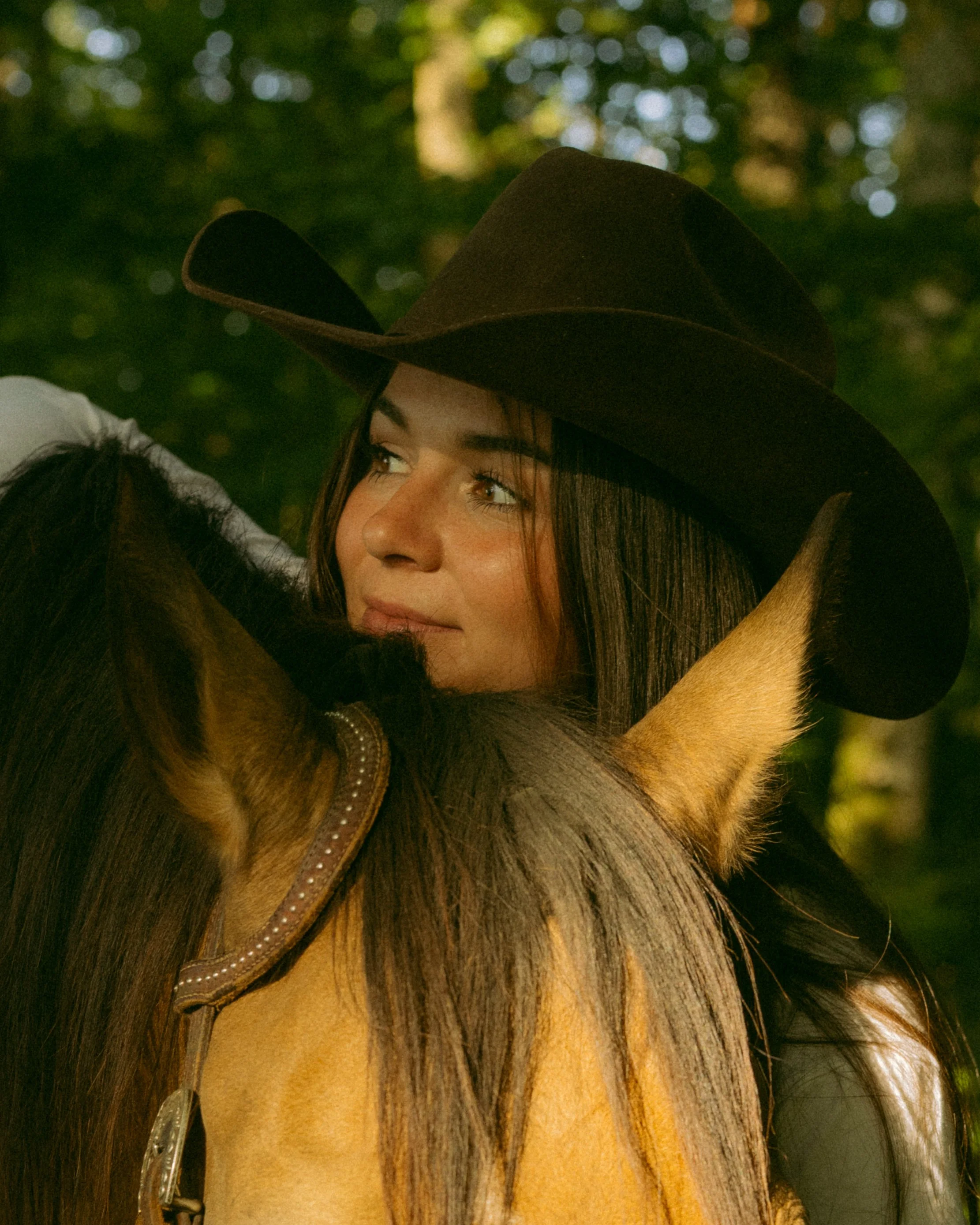 Nahaufnahme eines Mädchens mit braunen Haaren, das einen braunen Cowboyhut trägt, im Freien bei Sonnenlicht.