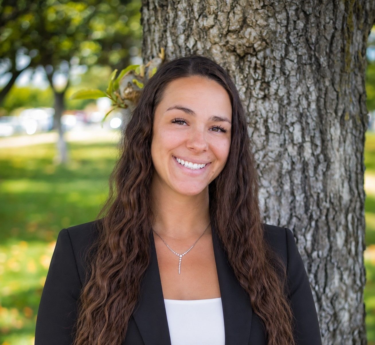 Kayla Roslan, a smiling young woman with long wavy hair, stands in front of a tree.