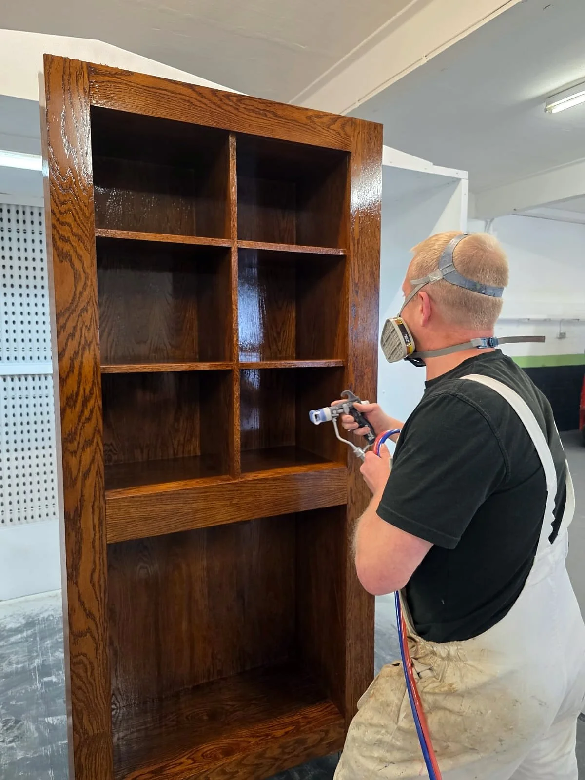 Spray finisher applying a gloss coat to a stained timber bookcase in the booth