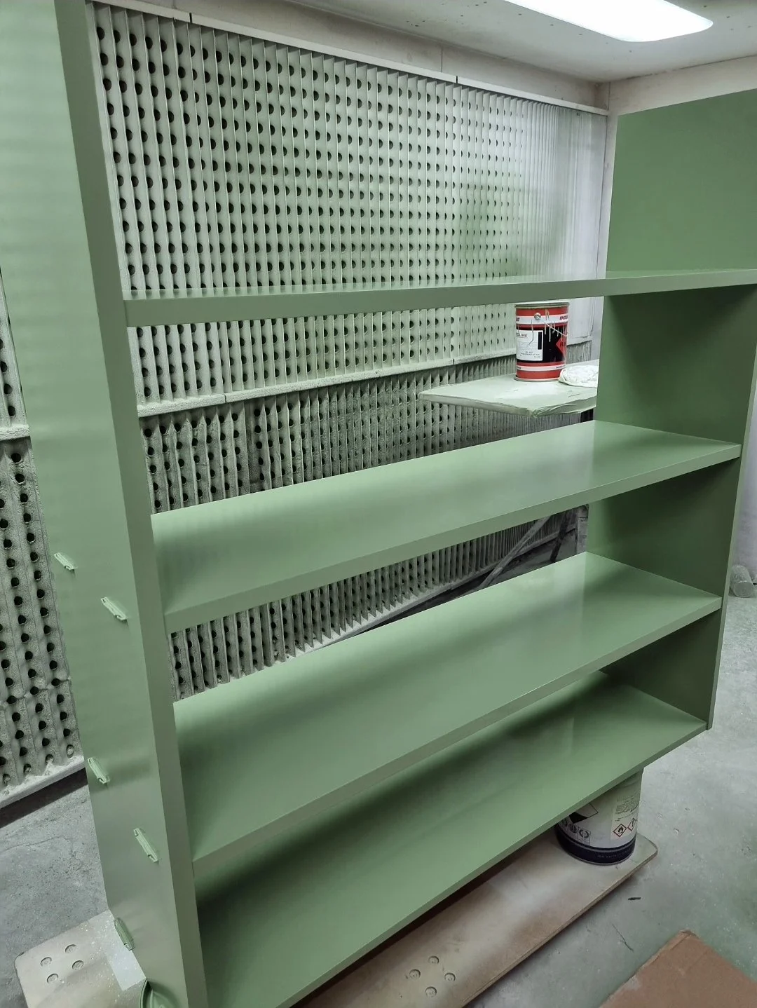 Open shelving unit sprayed in sage green, in the spray booth