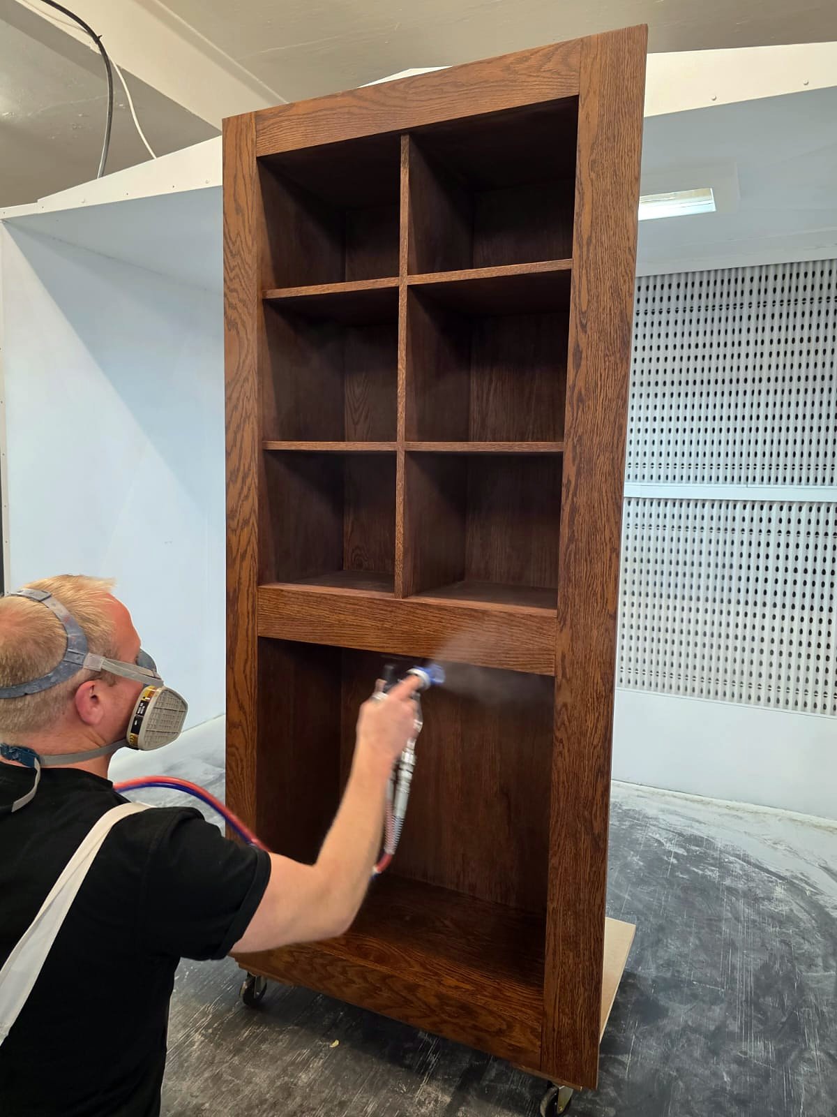 Spray finisher applying stain to a timber bookcase in the booth