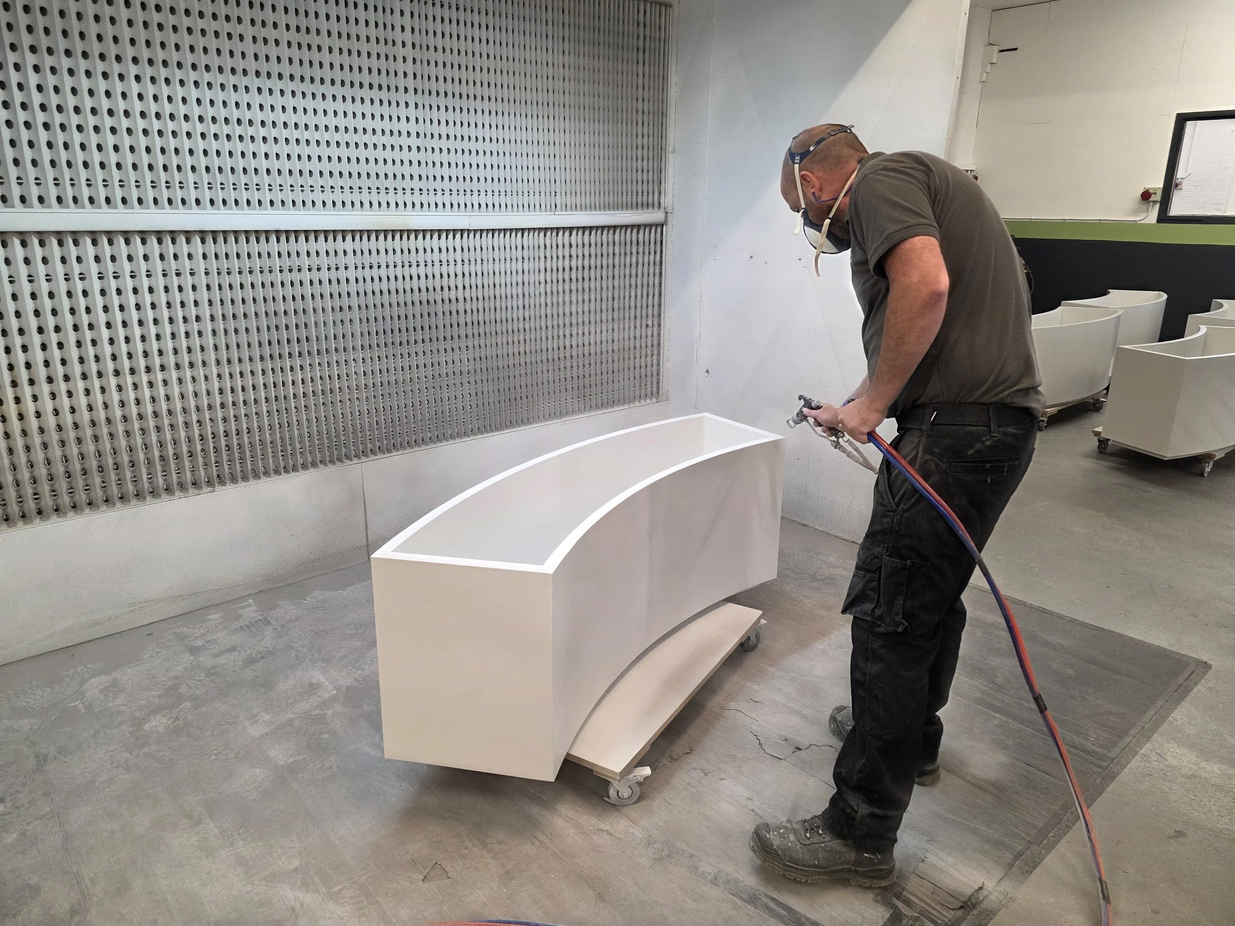 Spray finisher in a mask applying a white finish to a curved unit in the spray booth