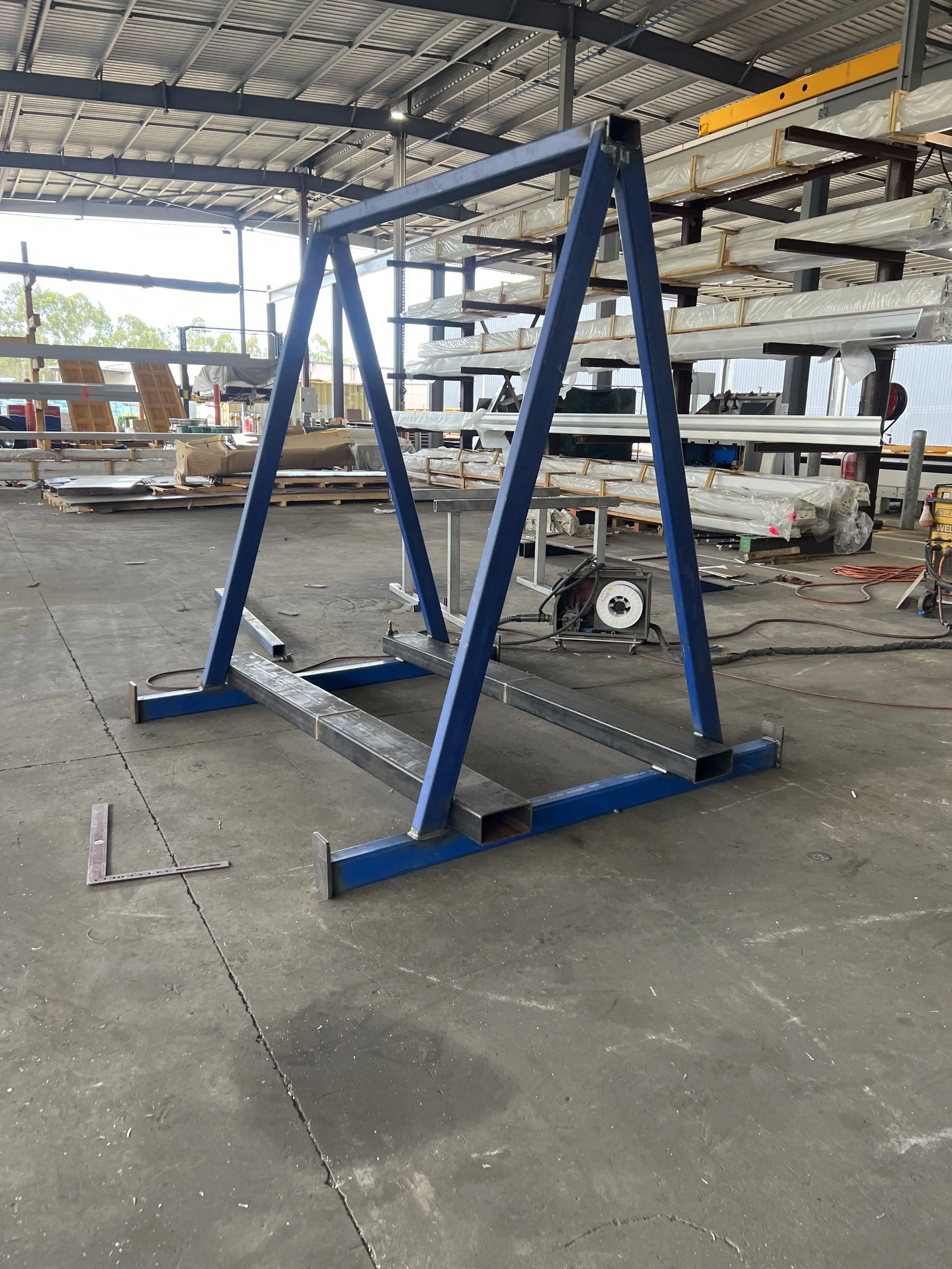 Empty warehouse or industrial workshop with metal shelving, materials, and a blue metal A-frame structure in the foreground.