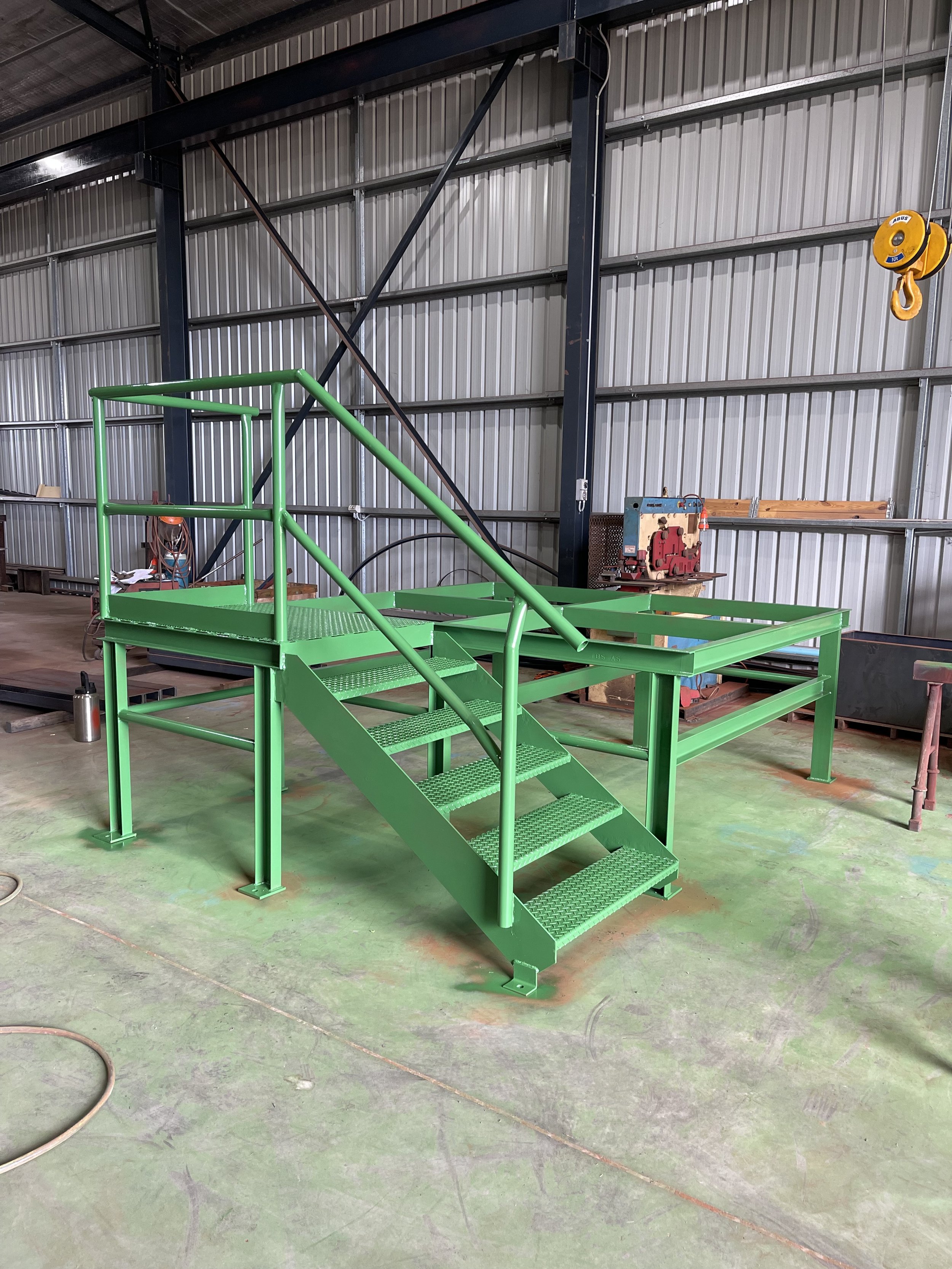 Green metal staircase with railings inside an industrial warehouse with corrugated metal walls.