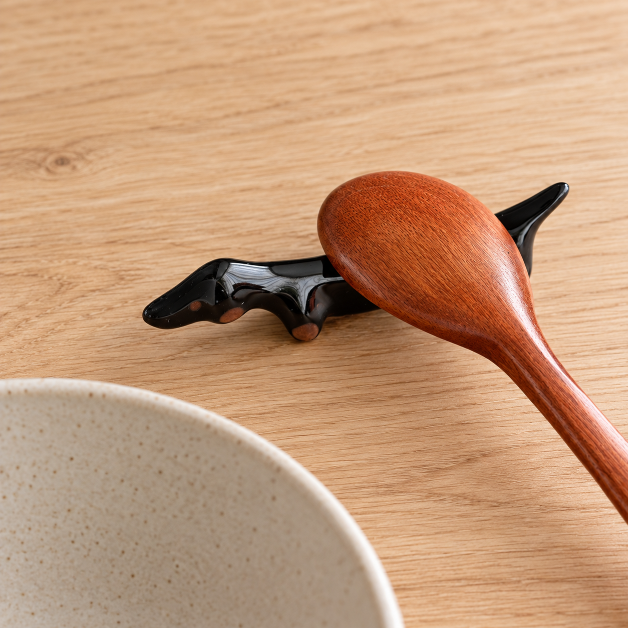 Black ceramic dachshund-shaped chopstick rest with dark wooden chopsticks on a light wood table.