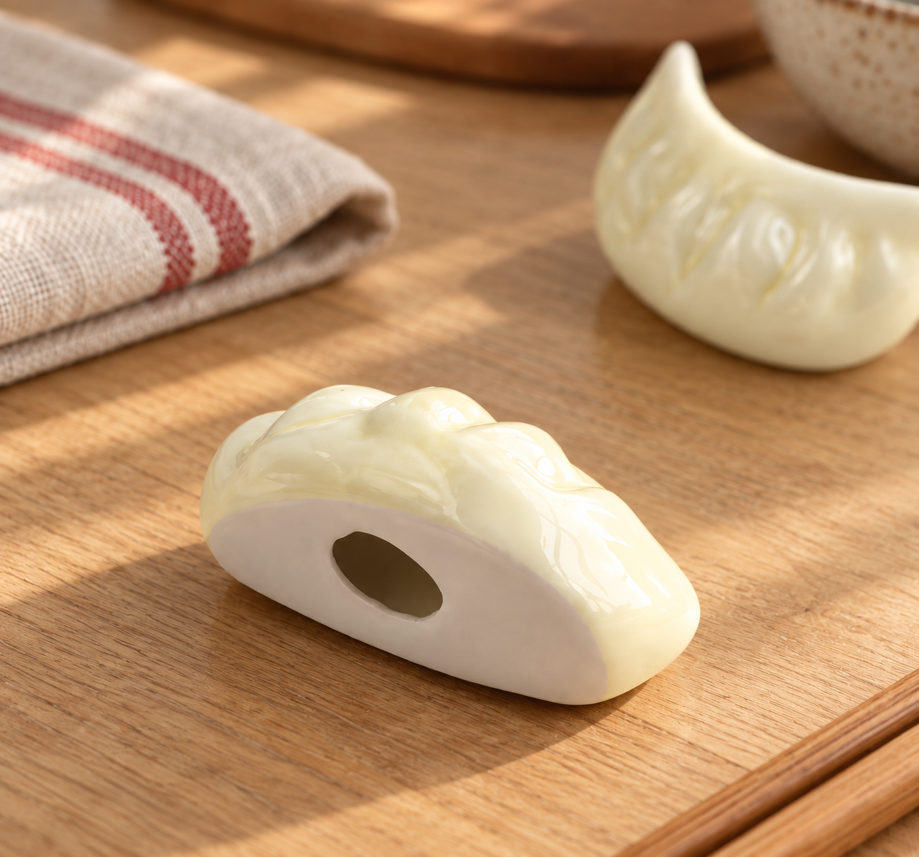 Ivory ceramic dumpling-shaped chopstick rests displayed on a warm wooden table in natural sunlight.