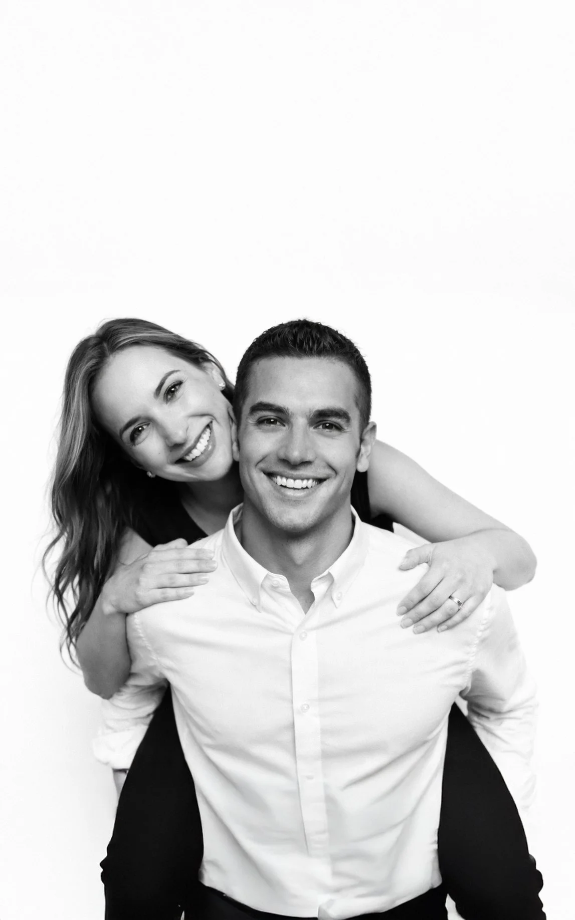 A black and white photo of a woman giving a piggyback ride to a man, both smiling.